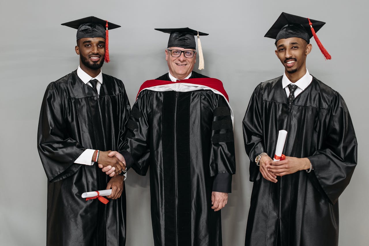 Three individuals in graduation attire celebrating success together indoors.